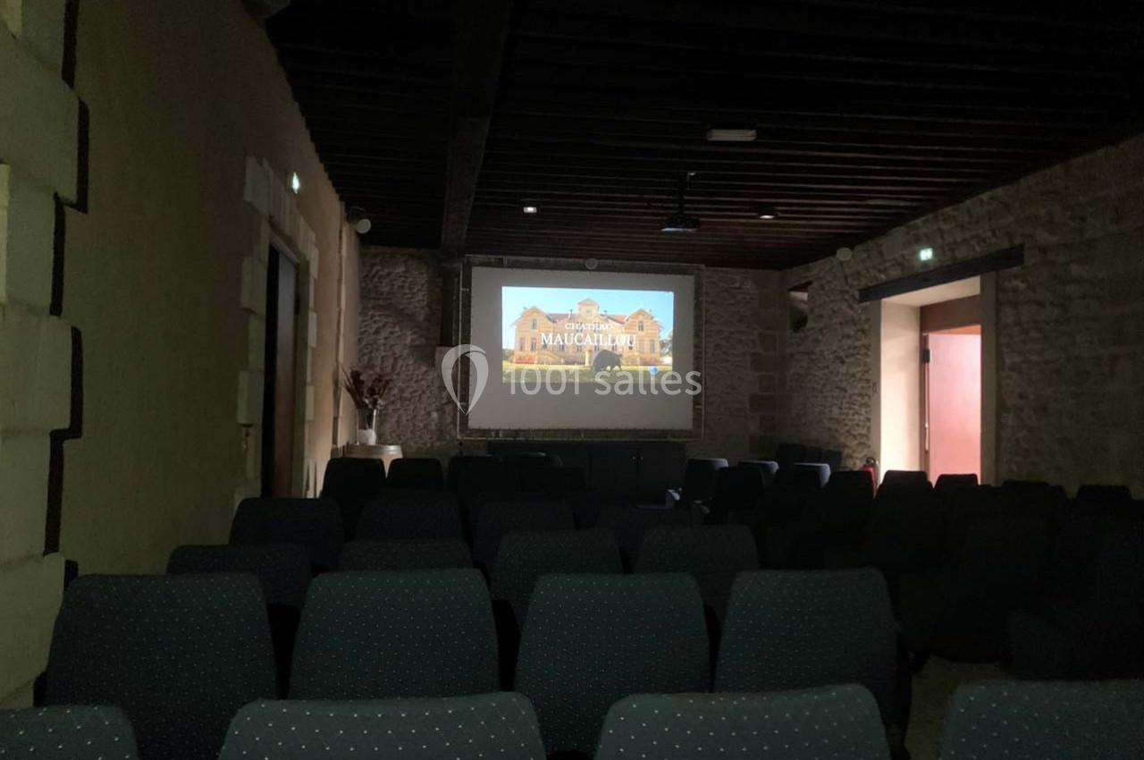 Salle sombre avec rangées de sièges vides, écran de projection affichant une image d'un bâtiment ancien.