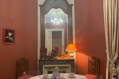 Grande table dressée avec nappes blanches, chaises blanches et chandeliers, dans une salle en pierre avec cheminée.