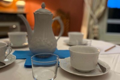 Grande table dressée avec nappes blanches, chaises blanches et chandeliers, dans une salle en pierre avec cheminée.