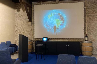 Grande table dressée avec nappes blanches, chaises blanches et chandeliers, dans une salle en pierre avec cheminée.