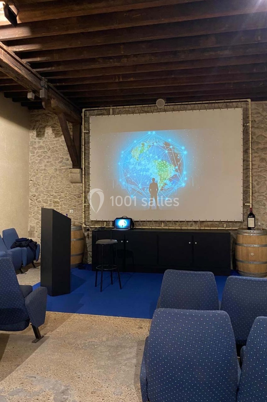 Salle de présentation avec écran projetant une image de réseau mondial, chaises bleues et tonneaux en arrière-plan.