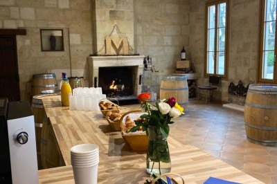 Grande table dressée avec nappes blanches, chaises blanches et chandeliers, dans une salle en pierre avec cheminée.