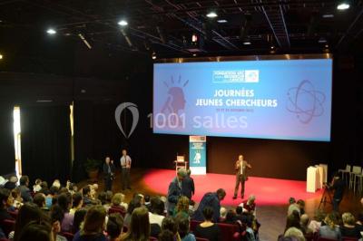 Pelouse avec des personnes assises ou allongées devant un grand bâtiment historique entouré d'arbres.
