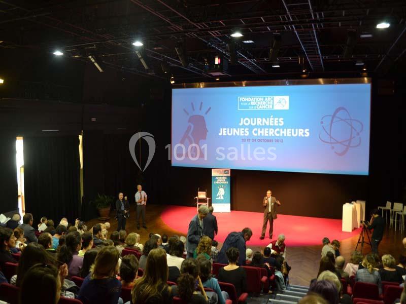 Conférence avec un intervenant sur scène devant un public, écran affichant ’Journées Jeunes Chercheurs’.