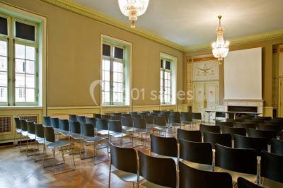 Pelouse avec des personnes assises ou allongées devant un grand bâtiment historique entouré d'arbres.
