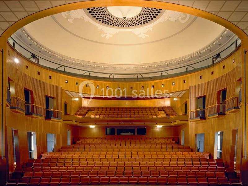 Vue intérieure d'un auditorium vide avec des sièges en bois, des balcons et un plafond décoratif circulaire.