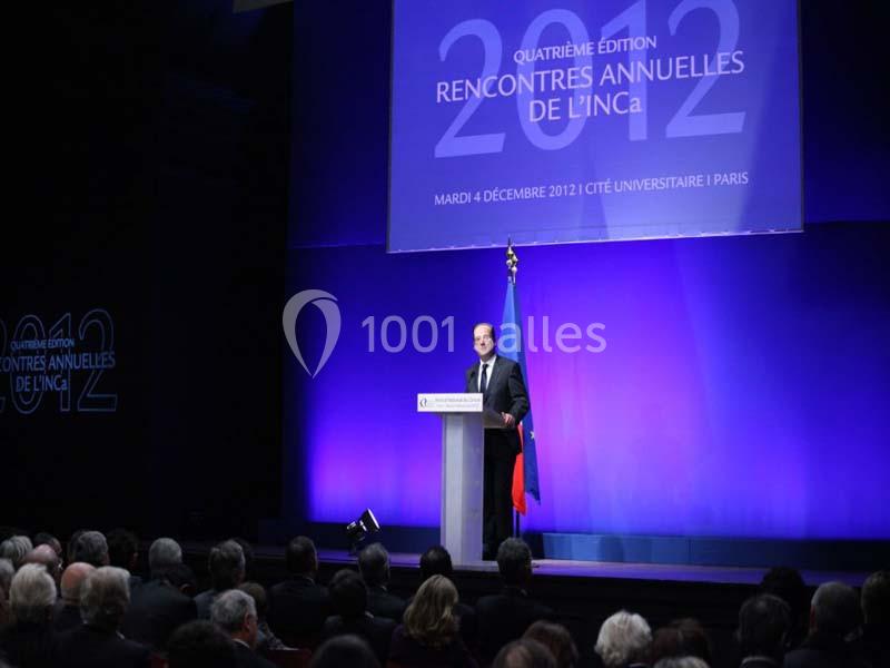 Un orateur s'exprime sur une scène devant un public, avec un écran affichant ’Rencontres annuelles de l'INCa 2012’.