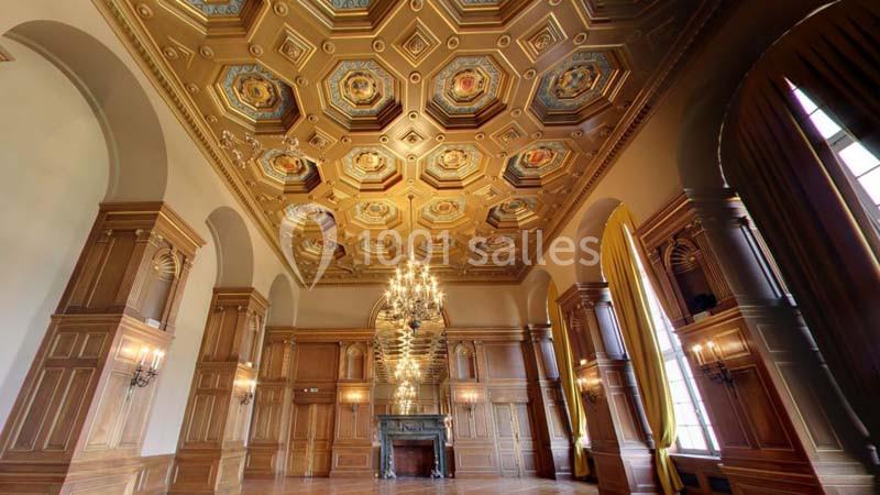 Plafond orné de motifs géométriques et peintures, lustre central imposant dans une salle aux boiseries élégantes.