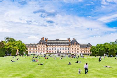 Pelouse avec des personnes assises ou allongées devant un grand bâtiment historique entouré d'arbres.