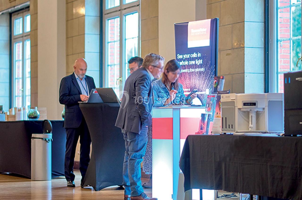 Des personnes interagissent autour d'un stand d'exposition technologique dans un espace intérieur lumineux.