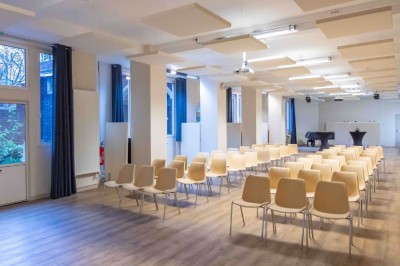 Façade d'un grand bâtiment historique avec un toit mansardé, entouré d'une pelouse où des personnes se détendent.