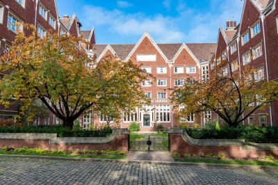 Façade d'un grand bâtiment historique avec un toit mansardé, entouré d'une pelouse où des personnes se détendent.