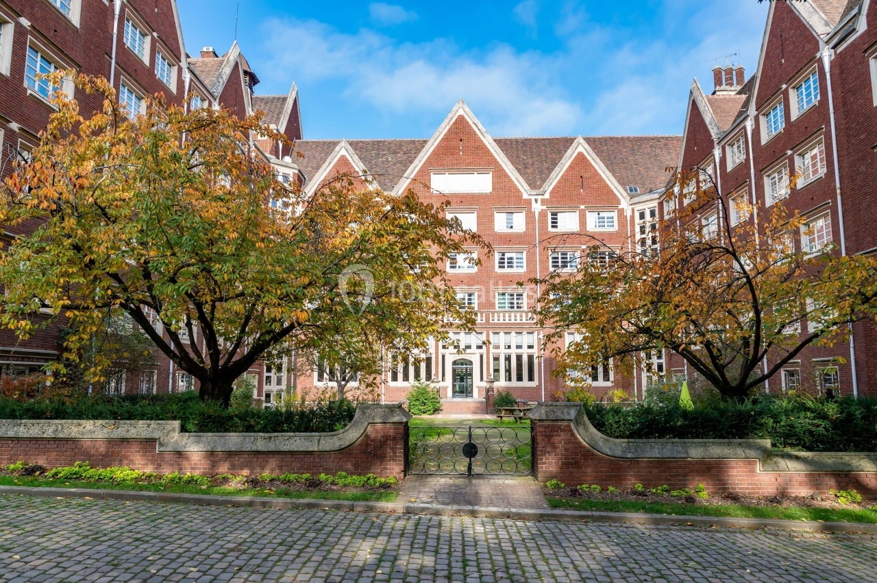 Cour pavée entourée de bâtiments en briques rouges avec des arbres aux feuilles d'automne et un ciel dégagé.