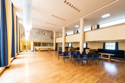 Façade d'un grand bâtiment historique avec un toit mansardé, entouré d'une pelouse où des personnes se détendent.