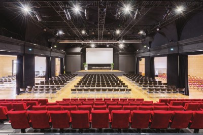 Façade d'un grand bâtiment historique avec un toit mansardé, entouré d'une pelouse où des personnes se détendent.