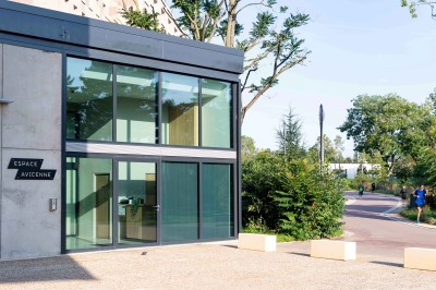 Façade d'un grand bâtiment historique avec un toit mansardé, entouré d'une pelouse où des personnes se détendent.
