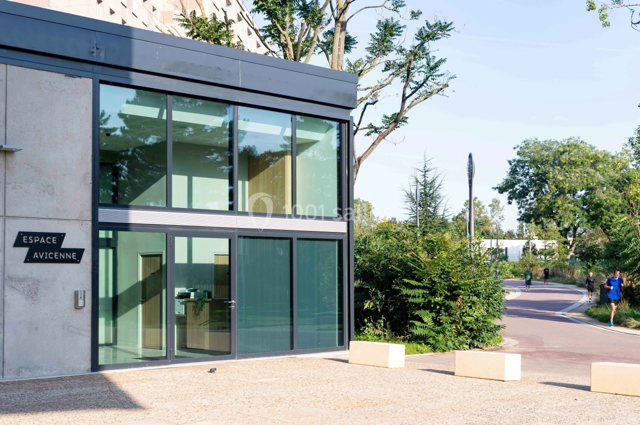 Façade vitrée d'un bâtiment moderne avec un panneau ’Espace Avicenne’, entourée de végétation et d'une route.