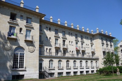 Façade d'un grand bâtiment historique avec un toit mansardé, entouré d'une pelouse où des personnes se détendent.