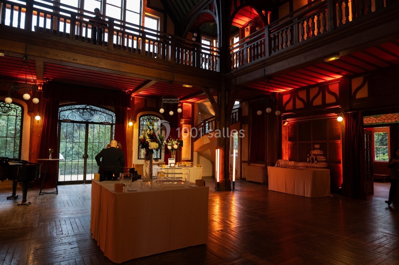Salle en bois avec éclairage chaleureux, tables dressées et grandes fenêtres donnant sur un extérieur verdoyant.