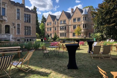 Façade d'un grand bâtiment historique avec un toit mansardé, entouré d'une pelouse où des personnes se détendent.