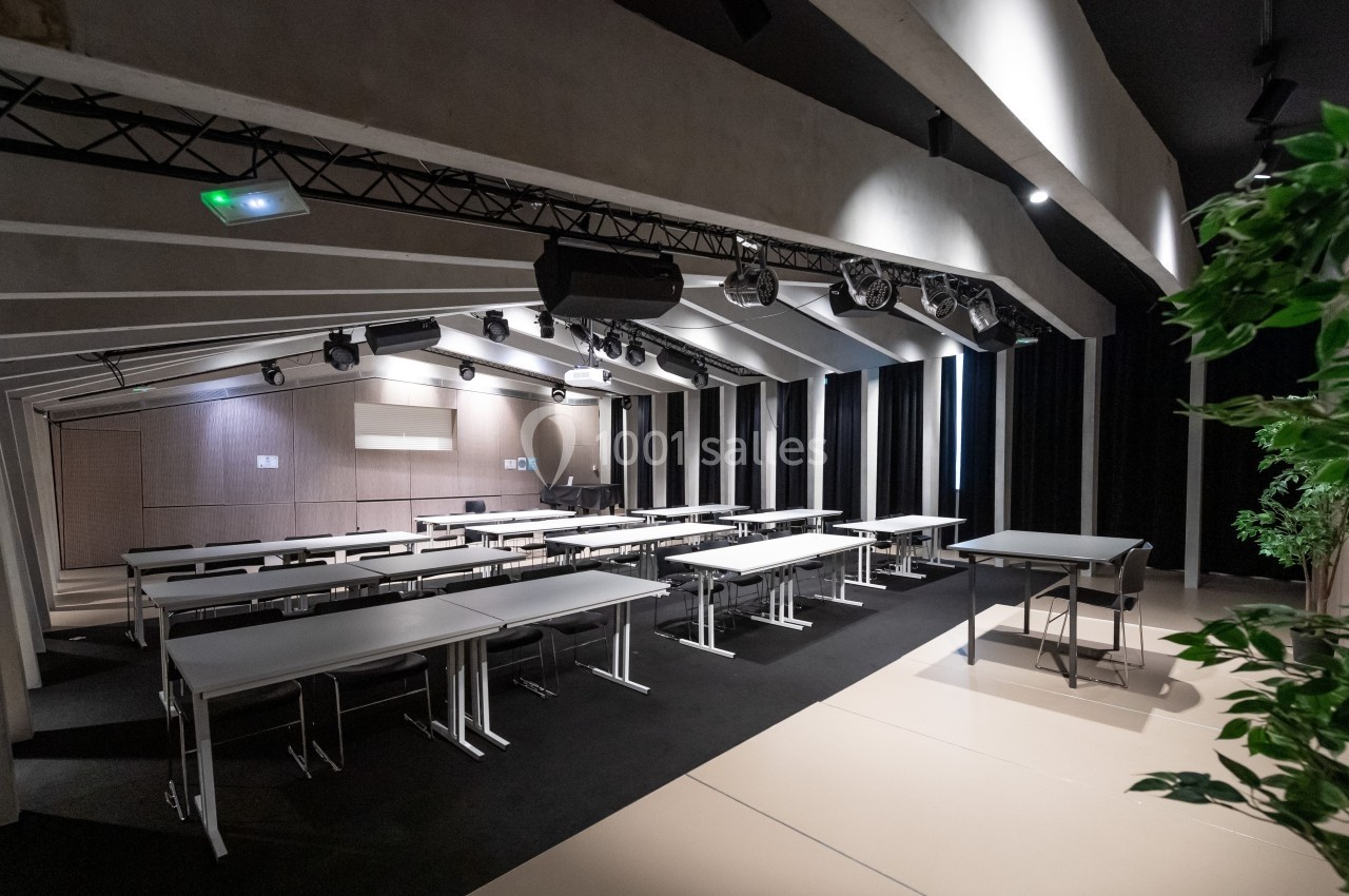 Salle de conférence moderne avec des tables et des chaises alignées, éclairage suspendu et plantes en décoration.