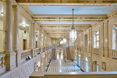 Façade d'un grand bâtiment historique avec un toit mansardé, entouré d'une pelouse où des personnes se détendent.