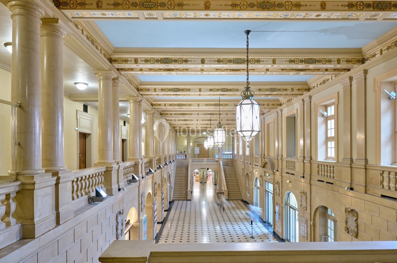Hall intérieur spacieux avec colonnes en pierre, plafond orné de motifs dorés et grandes lanternes suspendues.