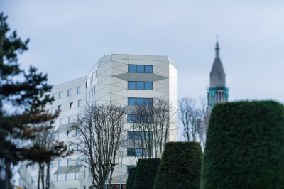 Façade d'un grand bâtiment historique avec un toit mansardé, entouré d'une pelouse où des personnes se détendent.