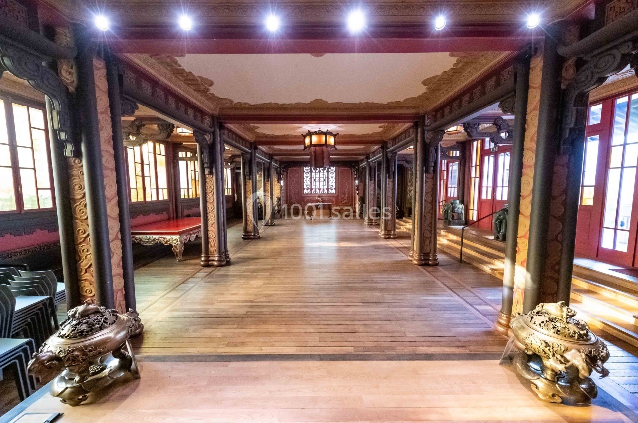 Salle intérieure ornée de colonnes sculptées, avec un parquet en bois et des fenêtres laissant entrer la lumière naturelle.