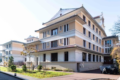 Façade d'un grand bâtiment historique avec un toit mansardé, entouré d'une pelouse où des personnes se détendent.