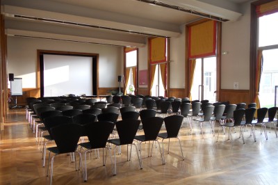 Façade d'un grand bâtiment historique avec un toit mansardé, entouré d'une pelouse où des personnes se détendent.