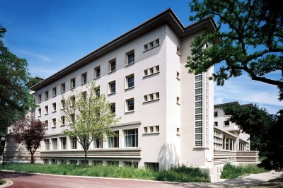 Façade d'un grand bâtiment historique avec un toit mansardé, entouré d'une pelouse où des personnes se détendent.