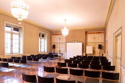 Façade d'un grand bâtiment historique avec un toit mansardé, entouré d'une pelouse où des personnes se détendent.