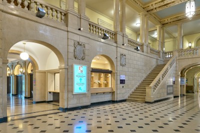 Façade d'un grand bâtiment historique avec un toit mansardé, entouré d'une pelouse où des personnes se détendent.