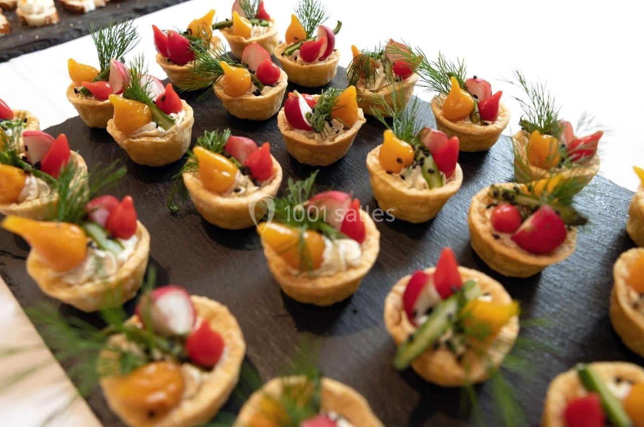 Plateau de mini-tartelettes garnies de légumes colorés, herbes fraîches et fromage, disposées sur une ardoise noire.