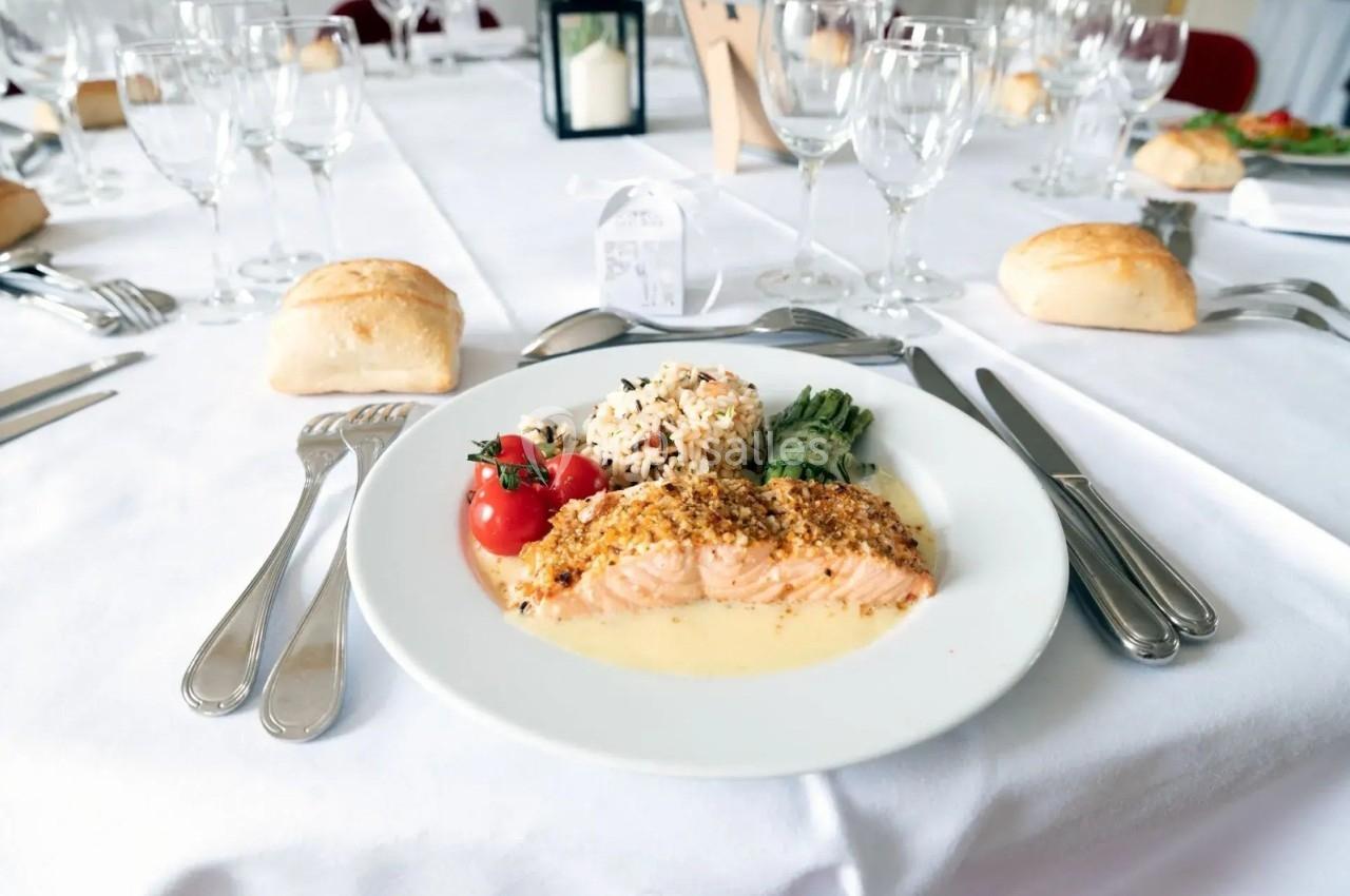 Assiette de saumon en sauce avec riz, légumes et tomates cerises, servie sur une table dressée avec couverts et verres.
