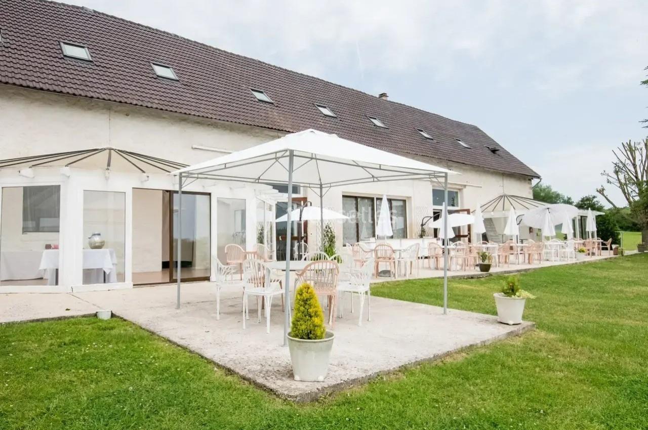 Terrasse extérieure avec tables et chaises sous des tonnelles blanches, devant un grand bâtiment à toit en pente.