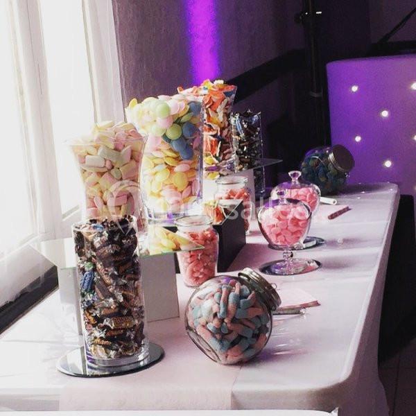 Buffet de bonbons colorés disposés dans des bocaux en verre sur une table blanche près d'une fenêtre.