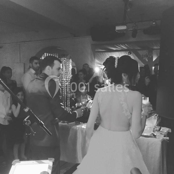 Un couple en tenue de mariage se tient devant une table lors d'une réception, entouré d'invités.