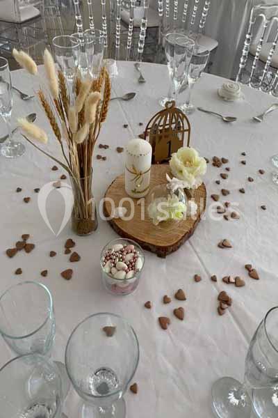 Table décorée pour un événement avec bougies, fleurs, rondin de bois et petits cœurs dispersés sur une nappe blanche.