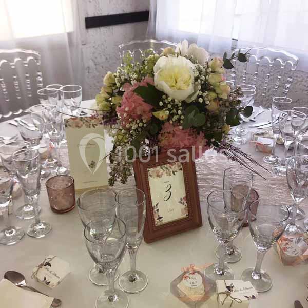 Table décorée pour un événement avec un centre de table floral, des verres, des menus et un cadre indiquant le numéro 3.