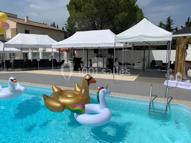 Bouées en forme de cygne et licorne flottant dans une piscine, avec des tentes blanches en arrière-plan.