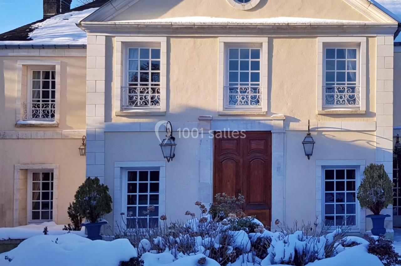 Façade d'une maison classique avec fenêtres à croisillons, porte en bois et jardin enneigé au premier plan.