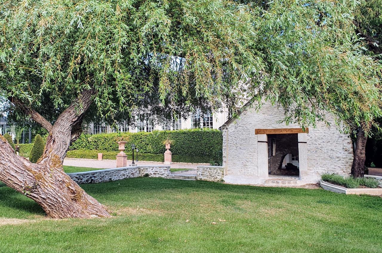 Petit bâtiment en pierre entouré d'herbe, d'arbres et de haies dans un jardin bien entretenu.