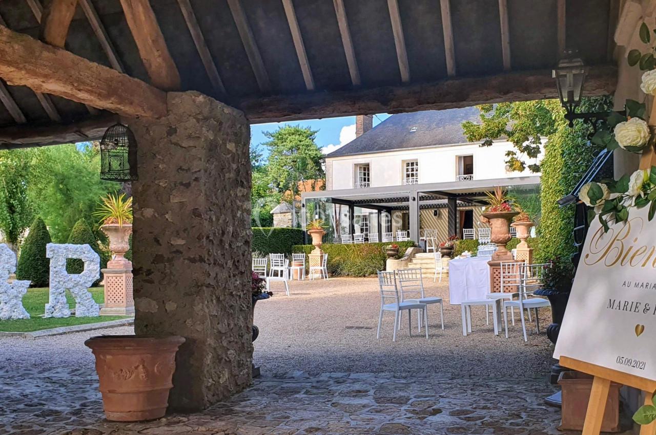 Entrée d'une cour décorée pour un mariage, avec une pancarte de bienvenue et des initiales fleuries.