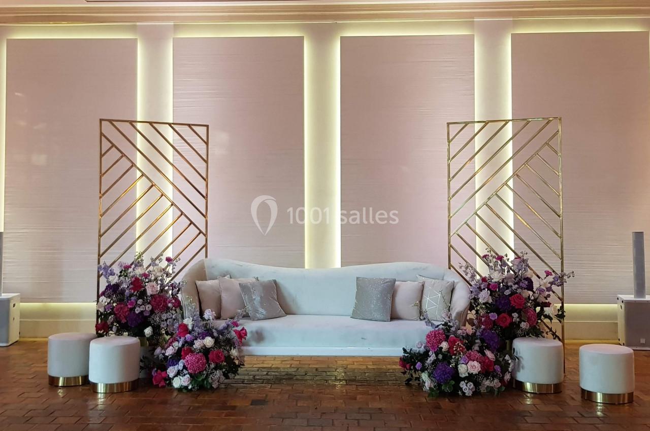 Canapé blanc entouré de compositions florales colorées et de panneaux dorés, dans un décor lumineux et épuré.