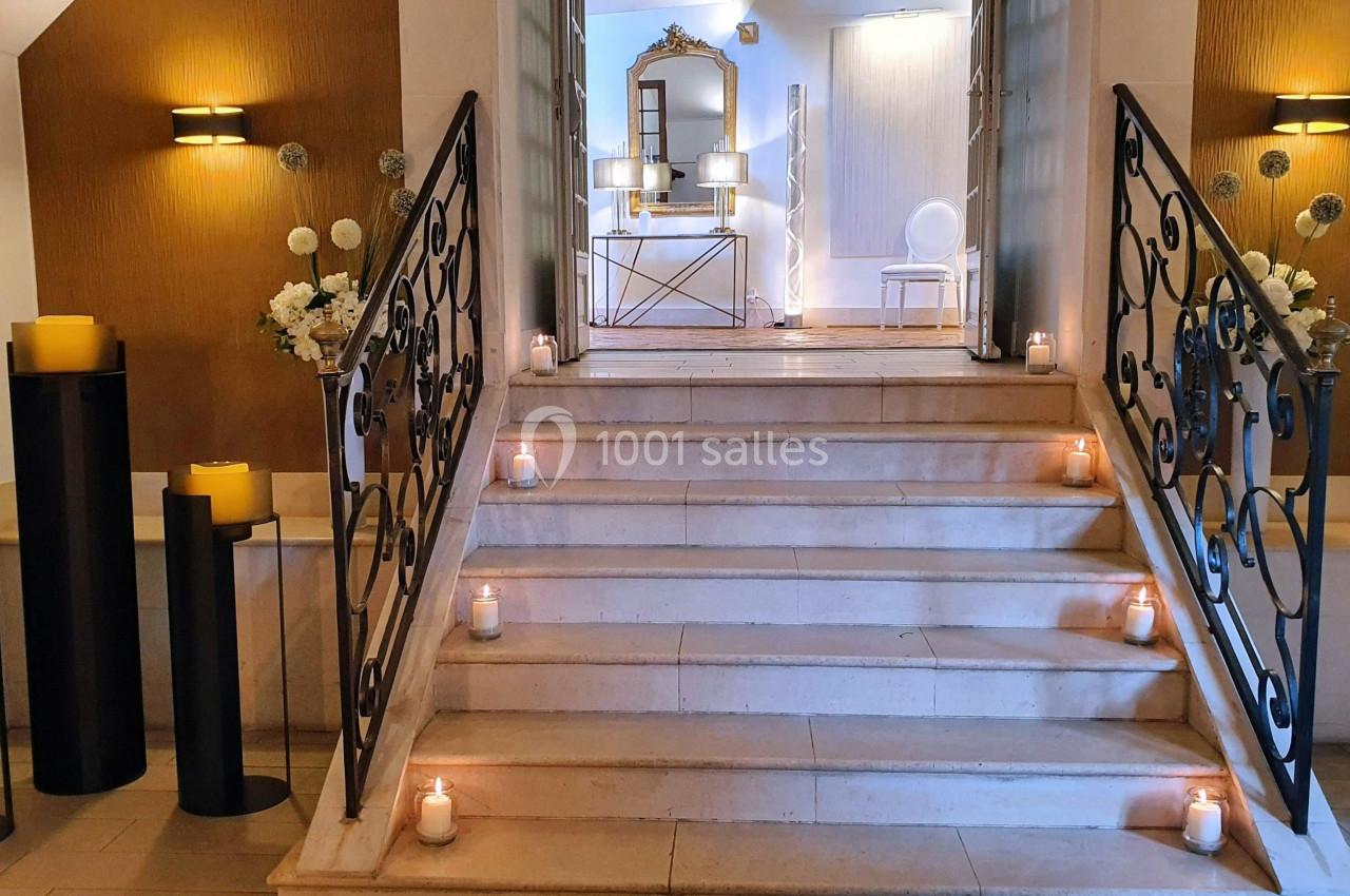 Escalier en pierre décoré de bougies allumées, menant à une pièce lumineuse avec miroir et chaise blanche.