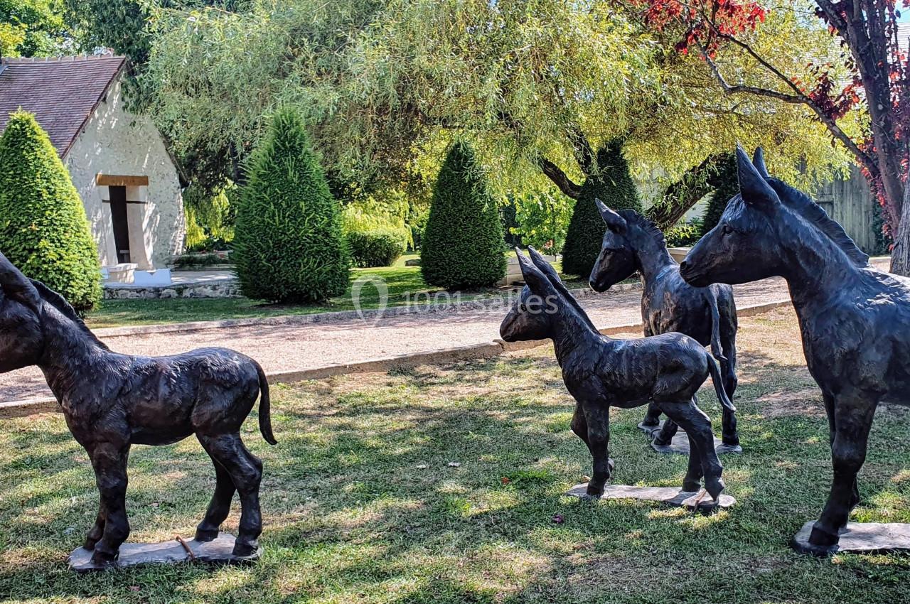 Statues en bronze de quatre ânes sur une pelouse, entourées d'arbres et d'arbustes dans un jardin.