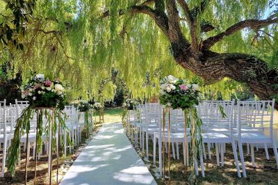 Couronne de fleurs blanches et roses suspendue à un arbre sous la lumière du soleil dans un jardin verdoyant.
