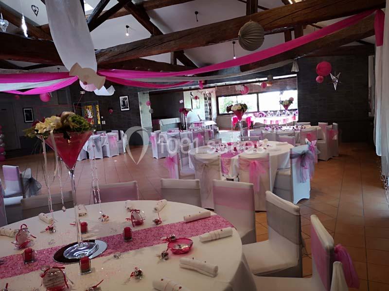 Salle de réception décorée avec des nappes blanches, des rubans roses et des compositions florales sur les tables.